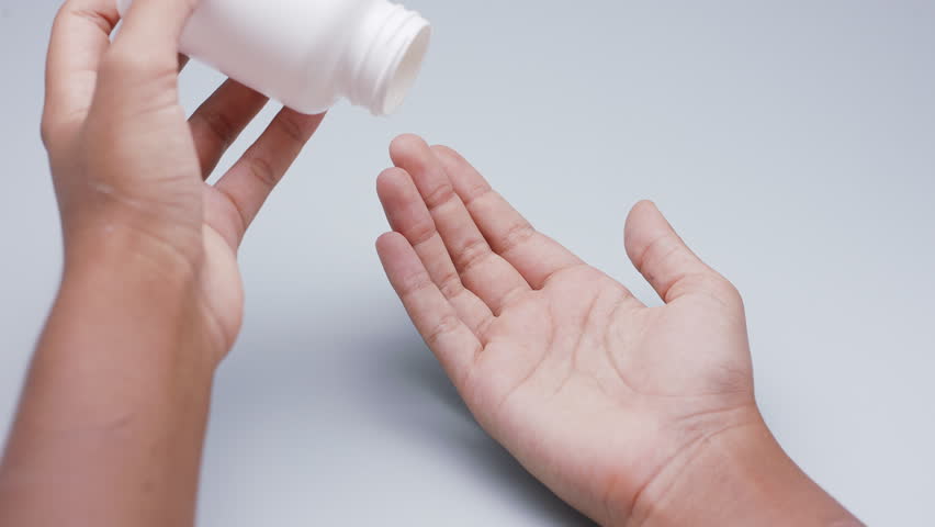 White capsules or pills being poured from a plastic bottle into a hand against a light gray background. Concept of medicine, healthcare, supplements, and pharmaceutical treatment.