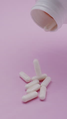 Slow motion video: white pills or capsules falling on a pink background. Concept of medicine, healthcare, supplements, and pharmaceutical treatment.