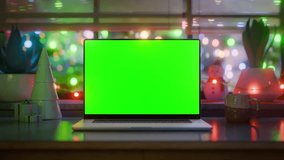 Laptop with green screen mockup in cozy Christmas interior, blinking festive lights and falling snow outside the window, seamless looped video for holiday ads - Powered by Shutterstock - Get 15% off with code: PIKWIZARD15
