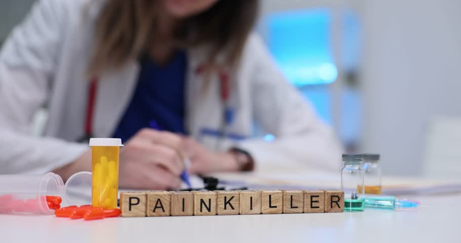 Woman reviews papers near Painkiller on blocks and colorful pills on desk. Focus on pain management highlights administration and prescription