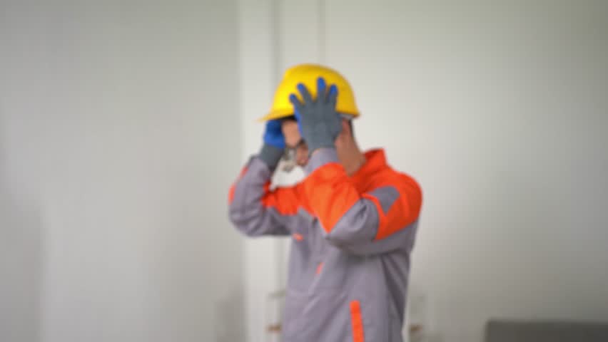 A construction worker carefully adjusts his safety helmet and gloves indoors, displaying attention to safety in a dedicated work environment, emphasizing readiness.
