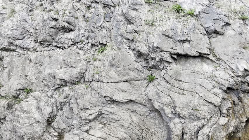 weathered stone cliff with natural cracks and sparse grass for rugged background or raw geology texture design