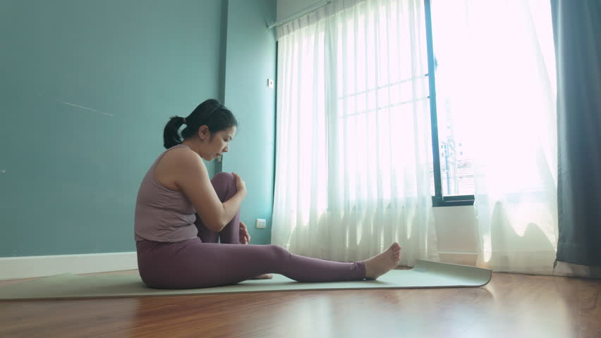 Asian Woman stretching on yoga mat at wooden floor during yoga class.