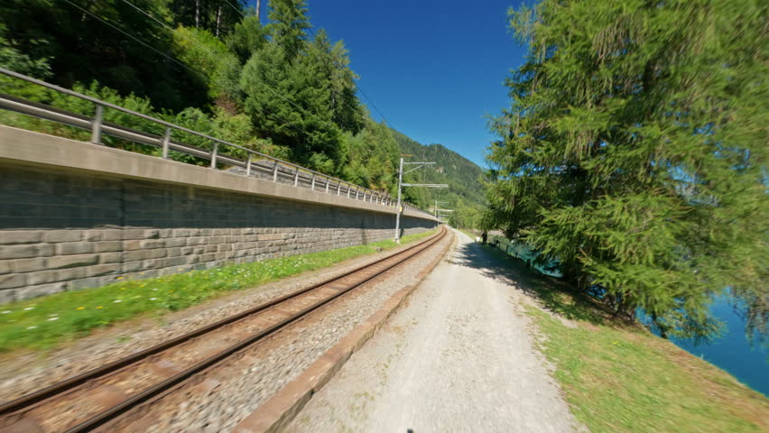 Train tracks curve by Poschiavo Lake under a bright blue sky