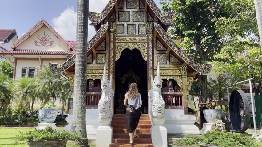 Tourist entering Wat Phra Singh temple in Chiang Mai, Thailand, with ornate golden architecture, guardian statues, and traditional Lanna design
