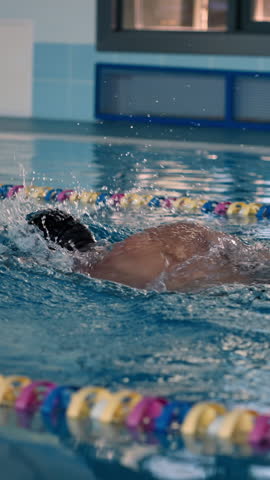 Professional swimmer trains Crawl stroke in fresh pool water. Strong sportsman swims along separated lane in large swimpool at athletic center