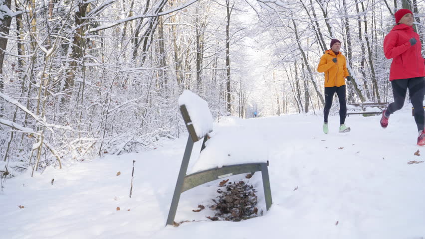Smiling middle-aged trail running couple man and woman in bright windproof jackets jogging along snowy forest path on sunny frosty winter day. Sporty active people, outdoor training, 4K video - Powered by Shutterstock - Get 15% off with code: PIKWIZARD15