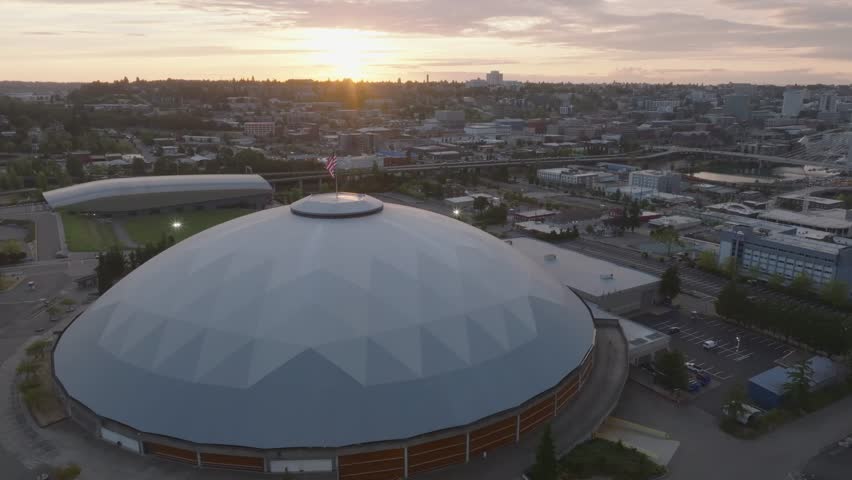 Aerial view of the Tacoma Dome, its stark white dome contrasting with the city skyline under a vibrant sunset sky, Tacoma, Washington, United States.