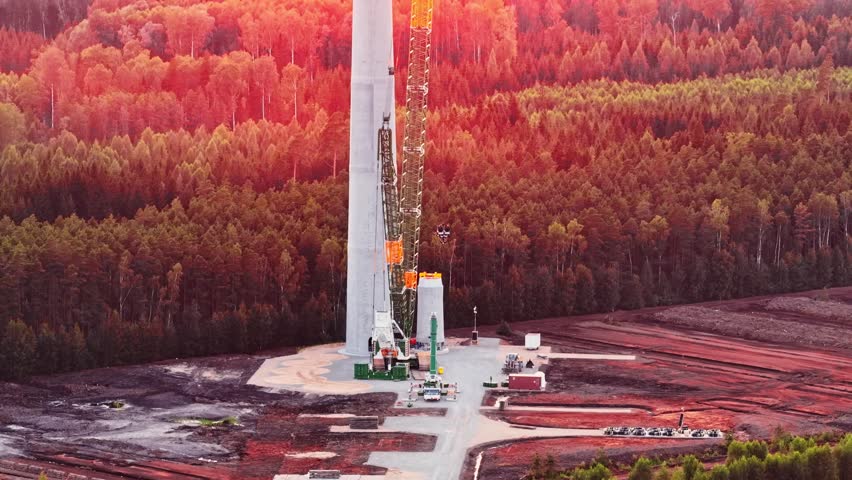 Aerial tilt up along wind turbine construction and crane on reddish fields with pink sky tones during sunset hours