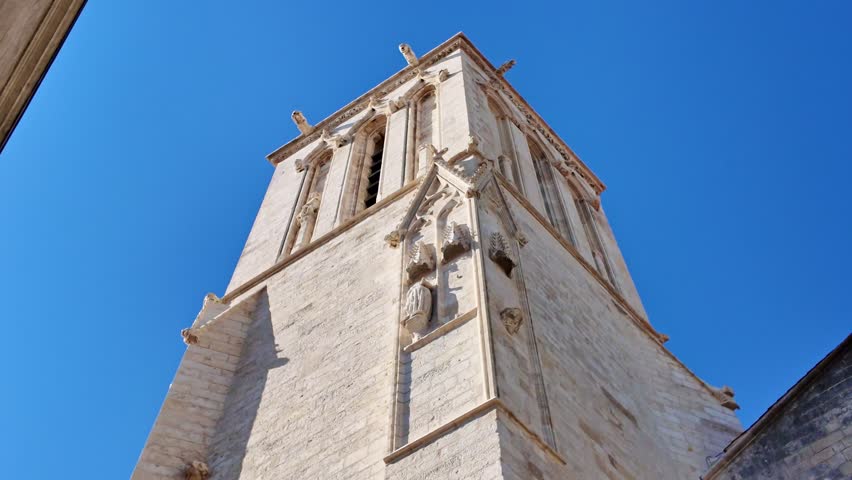 Low-angle view of historic Saint-Sauveur Church, detailed Gothic stone architecture, bell tower, arched windows, La Rochelle, France. Tilt-down