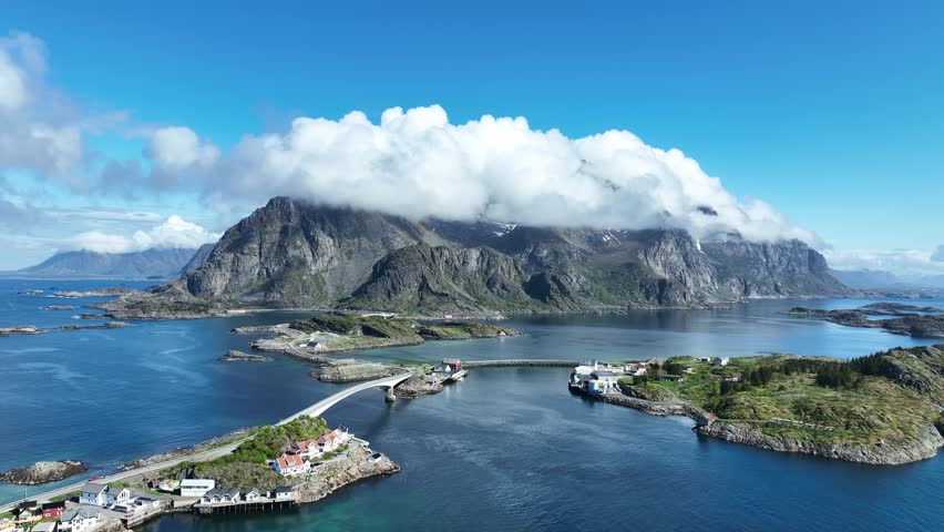 Drone flies forward over Henningsvaer road with bridges sea and mountains covered by clouds