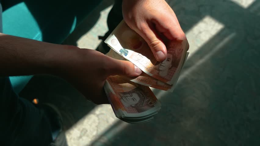 Male hands counting UK pounds bills close-up. Handling British currency in daylight. Managing ten and twenty pound banknotes indoors