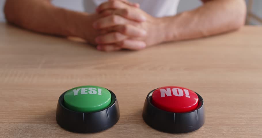 Closeup of a hand about to press a red NO button next to a green YES button on a wooden table, symbolizing choice, decision, and vote with a game buzzer feel. A hand chooses the no option.