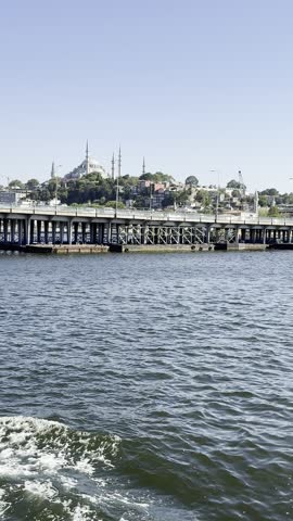 Atatürk Bridge (Atatürk Köprüsü) captured from moving yacht on Golden Horn estuary in Istanbul. Historic mosque rising above bridge, fishermen casting lines, cars and pedestrians crossing. Story, Reel