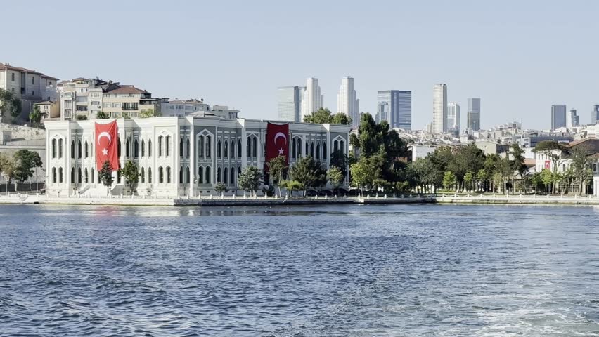 Sunlit view of Yıldız Palace’s Büyük Mabeyn Köşkü from yacht on Bosphorus, adorned with Turkish flags for July 15 Democracy and National Unity Day, skyscrapers in background. Cinematic video, Istanbul