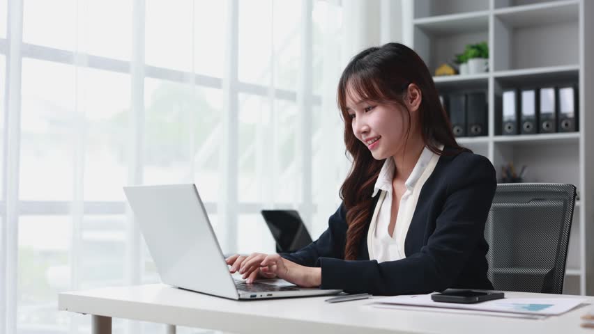 Confident Asian businesswoman working at sleek desk, typing on laptop with professional focus, illuminating modern office space with bright smile and professional energy