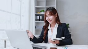 Professional businesswoman working at desk during video conference, taking notes with laptop, smiling confidently in modern office workspace - Powered by Shutterstock - Get 15% off with code: PIKWIZARD15