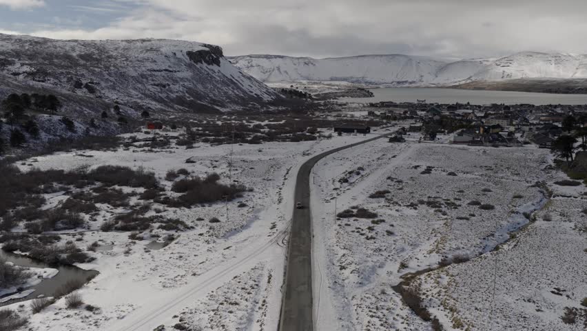 Descending aerial movement over the snowy road stretching through beautiful cold mountain valley towards Caviahue-Copahue, Nequén, Argentina.