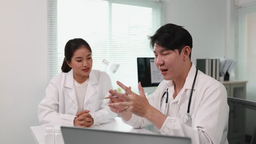 Two young asian doctors are discussing a diagnosis in a bright modern office, the male doctor is explaining something to his female colleague