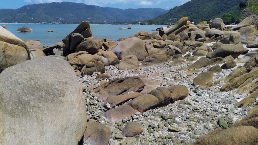 Aerial drone footage of Lamai Beach in Koh Samui, Thailand, featuring turquoise ocean, rocky shoreline, tropical island horizon, and scenic coastal landscape under clear tropical skies.