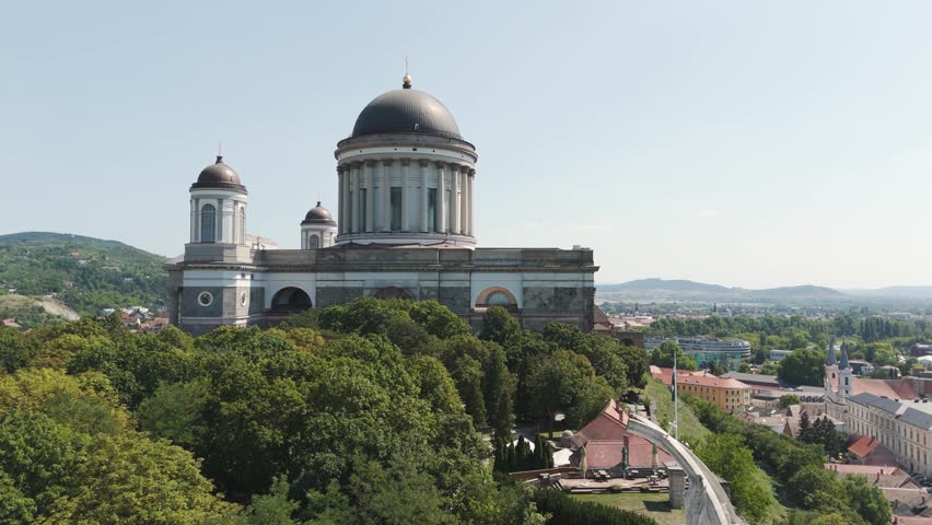 Aerial view of the Esztergom Basilica, a beautiful landmark in Hungary, surrounded by lush greenery. Pull Back Shot
