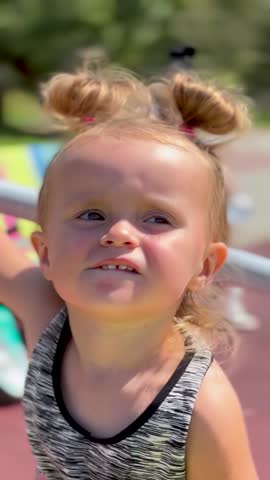 Little girl sitting on a playground carousel, enjoying the ride on a sunny day. Fun childhood, active play, and joy of movement