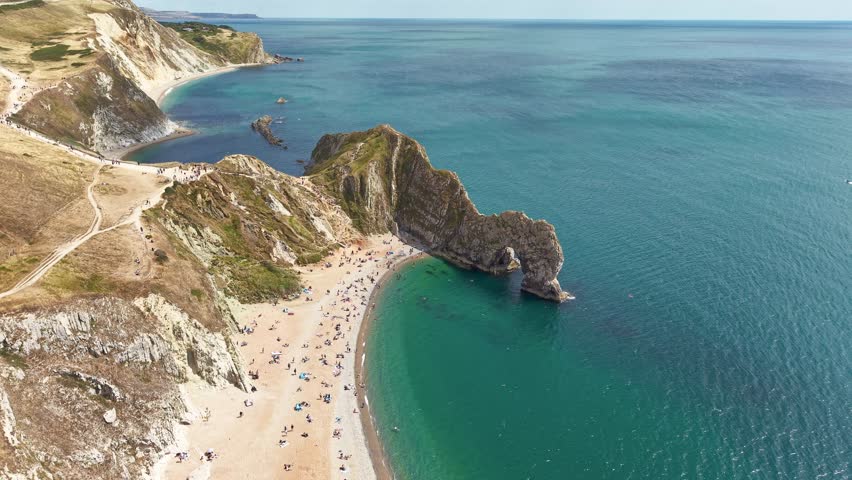 Orbiting view of people on the beach and swimming at Durdle Door in summer