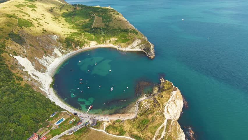 Circular bay with white cliffs, turquoise water and small village in England.