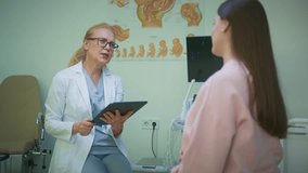 Caucasian doctor in white coat writing notes on digital tablet while talking with pregnant patient. Medical professional documenting examination results in consultation room with posters. - Powered by Shutterstock - Get 15% off with code: PIKWIZARD15