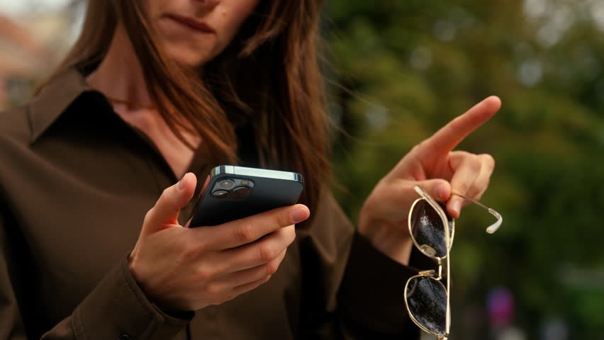Confused Caucasian woman with mobile phone lost direction in city searching location address outdoors using navigator looking around female using smartphone GPS service girl at street hold sunglasses
