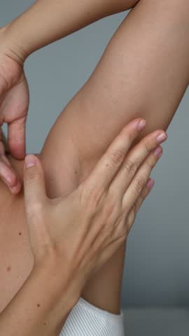 Vertical video of a young woman stroking the armpit showing her smooth skin after depilation on a grey background. The result of laser hair removal