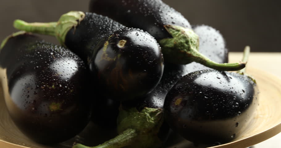 Fresh wet eggplants turning on light table against grey background, closeup