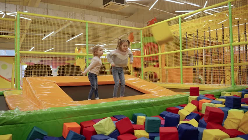 Two little girls playing on indoor playground in foam rubber pit in trampoline, active pastime in the amusement park. Slow motion