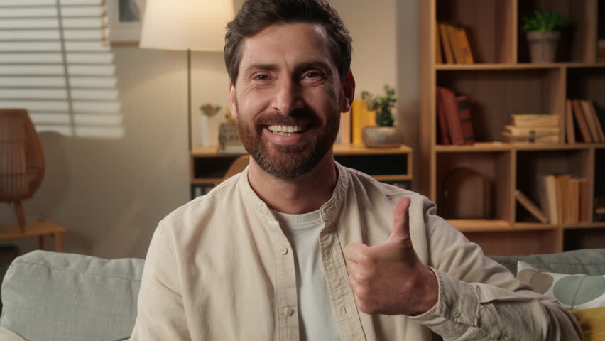 Caucasian man portrait at home casual living room smiling joyful male homeowner tenant freelancer businessman happy looking at camera thumb up recommend like gesture good excellent super approve sign