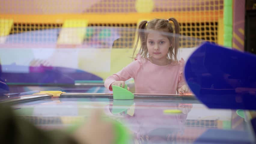 Happy little cute boy and girl playing air hockey arcade in game machine at modern game center. Slow motion