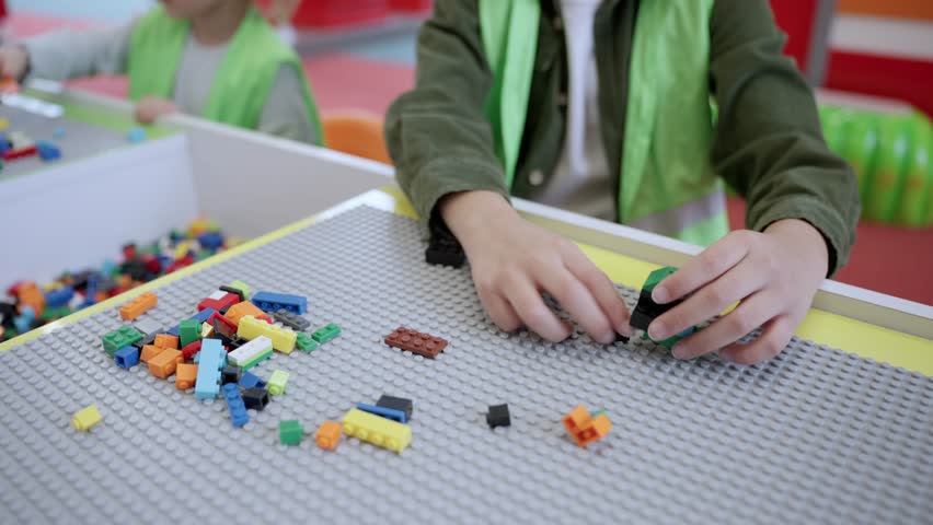 Children playing and building with colorful plastic bricks on the table, wearing waistcoat in game center. Slow motion