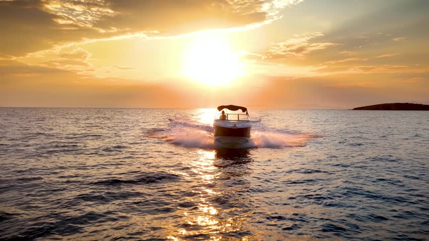 Front view of a motor speedboat cruising with speed over the ocean during golden summer sunset time
