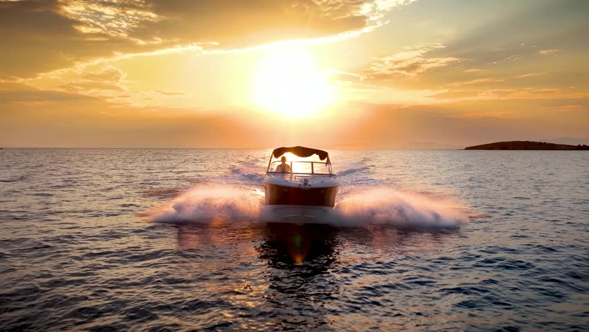 Front view of a motor speedboat cruising with speed over the ocean during golden summer sunset time
