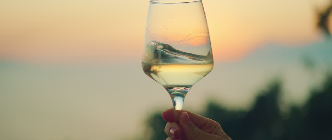 Wine glass held against colorful sunset sky and sea view in summer evening