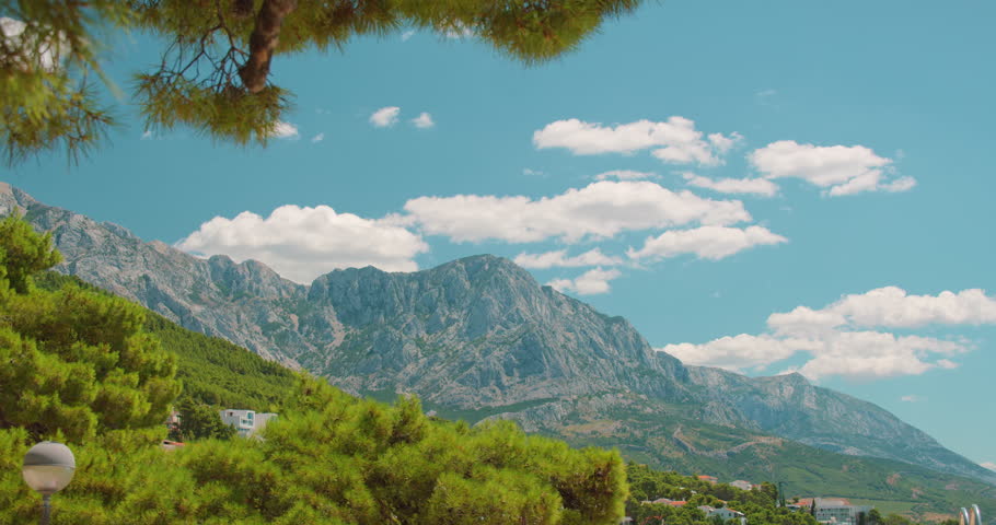 Mountain range under bright sky with scattered clouds and pine trees in Croatia