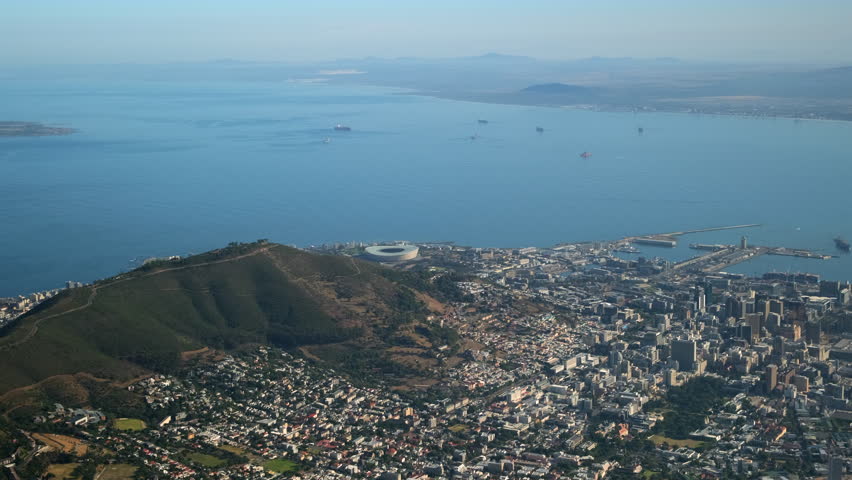 Wide aerial shot of Cape Town with coastline, Table Bay, and surrounding mountains. The cityscape reveals urban life, nature, and the harbor. Clear weather creates a peaceful, panoramic atmosphere
