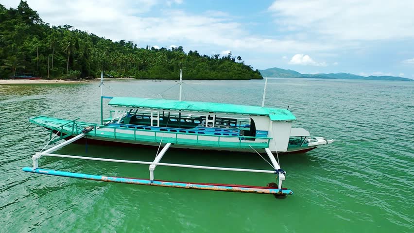 Traditional Filipino boat docked near forested tropical coast in Palawan, Philippines
