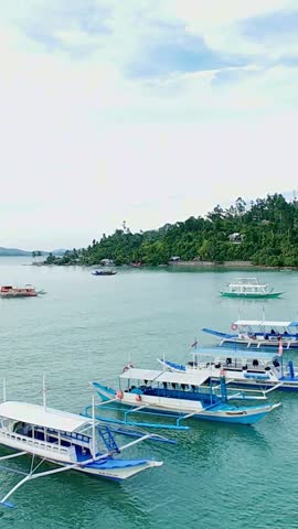 Vertical screen view of traditional Filipino boats moored in calm blue bay near Palawan, Philippines