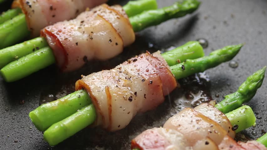 Tongs flipping Bacon and asparagus rolls on a hot pan.