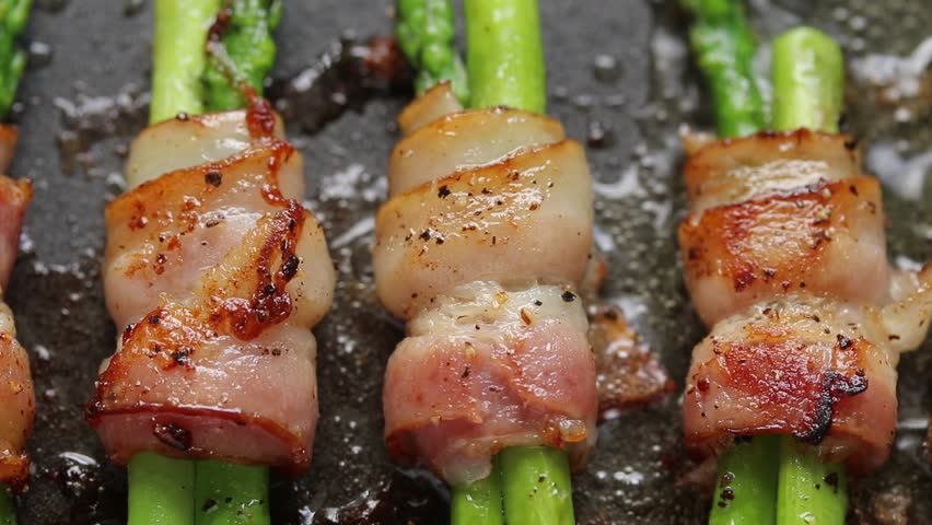 Bacon and asparagus rolls pan-fried with oil on a hot pan. Top view shot