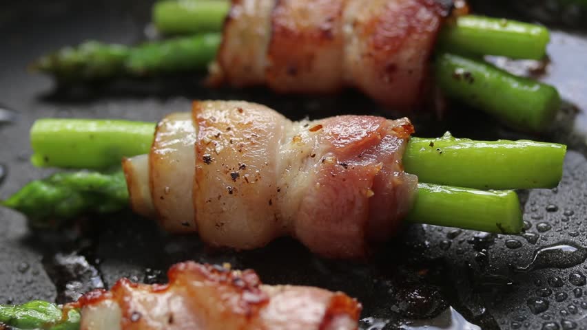 Bacon and asparagus rolls pan-fried with oil on a hot pan. Close-up view