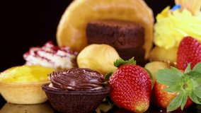 A variety of desserts including glazed donuts, cupcakes, brownies, tarts, and strawberries rotate under bright studio lighting against a dark, reflective backdrop - Powered by Shutterstock - Get 15% off with code: PIKWIZARD15