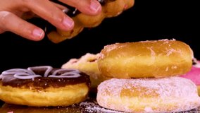 A hand reaches into a stack of assorted donuts, picking up a pink frosted ring donut. Bright studio lighting and black background highlight the vibrant colors - Powered by Shutterstock - Get 15% off with code: PIKWIZARD15