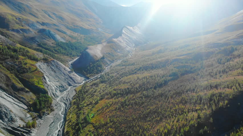 Sunlight illuminating mountain valley with river and conifer forest. Media