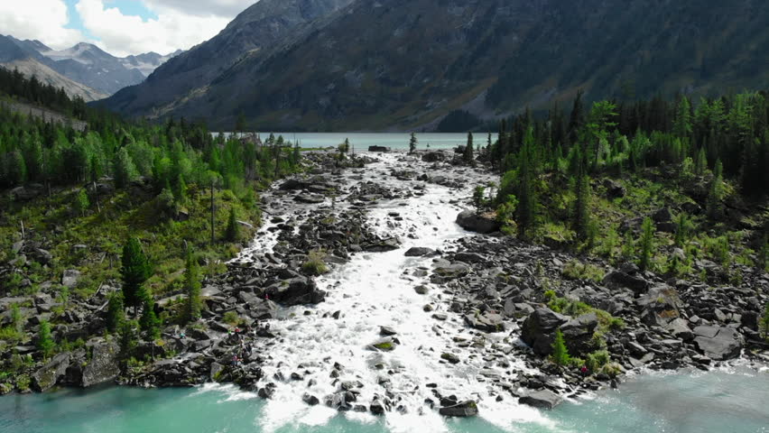 Turquoise mountain lake flows into a rocky river. Media
